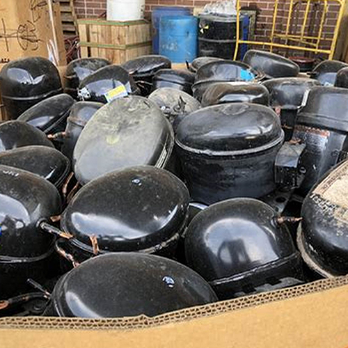 Black AC fridge compressors scrap metal in a brown carton.