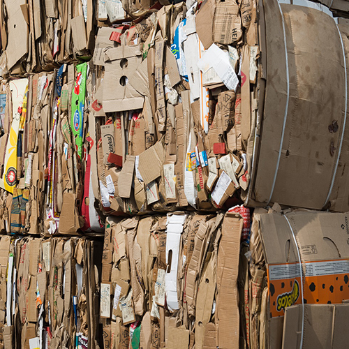 Compressed brown corrugated cardboard OCC waste paper scrap bundled and stacked up high. Click to inquire